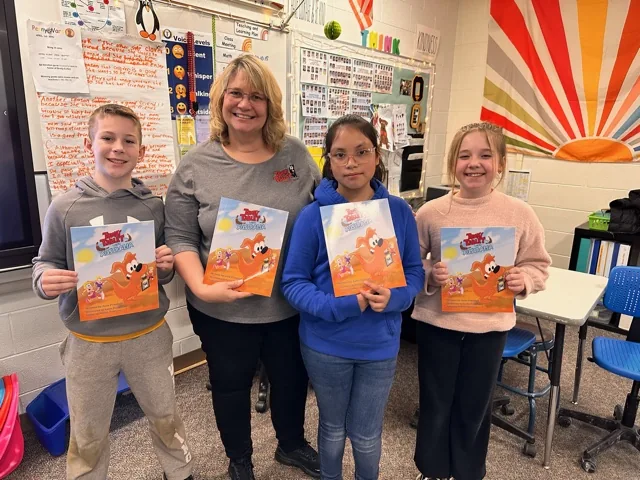 Julie Prantera in a classroom with three students, each holding Tommy Tablet Takes Australia.